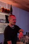 Bartender i svart tröja bakom en bar med flaskor och glas
