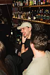 Man i keps samtalar vid bardisken på en bar.